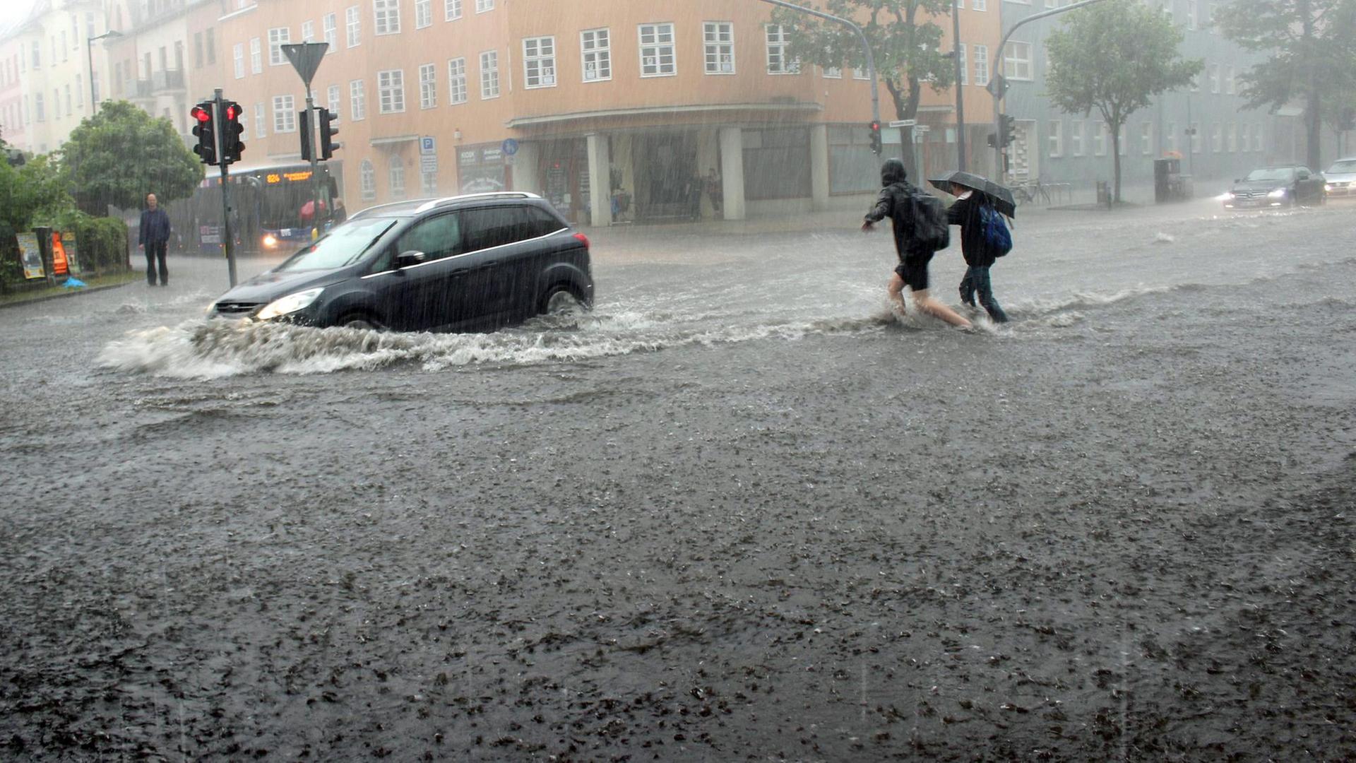 Eine überschwemmte Straße, auf der ein Auto fährt, dessen Reifen im Wasser versinken.